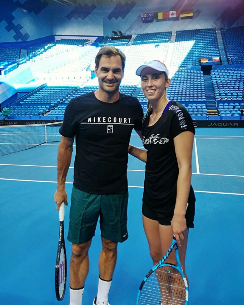 Elise Mertens and Roger Federer pose with rackets on blue indoor tennis court inspiring athletic spirit Wallpaper