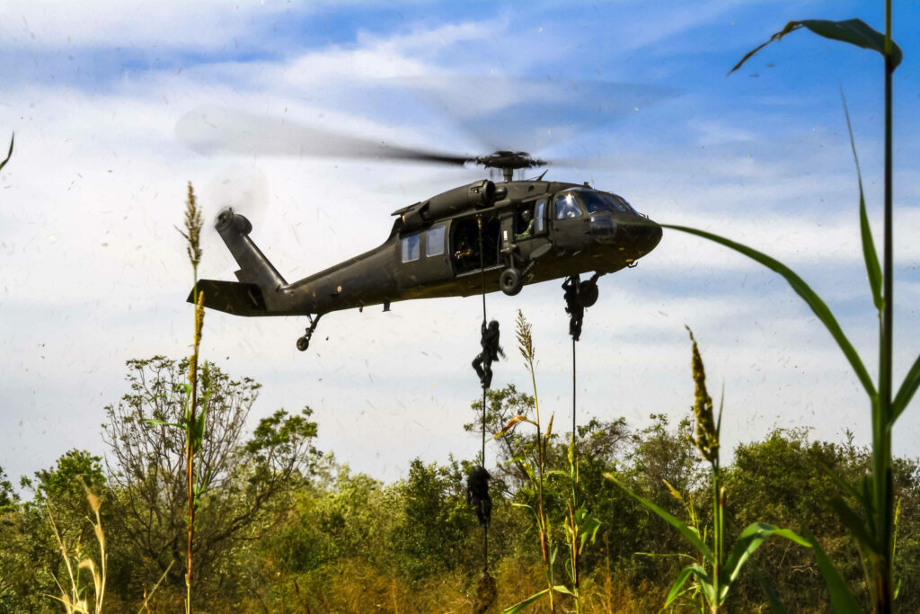 Soldiers rappelling from Black Hawk helicopter over dense green forest during military operation Wallpaper