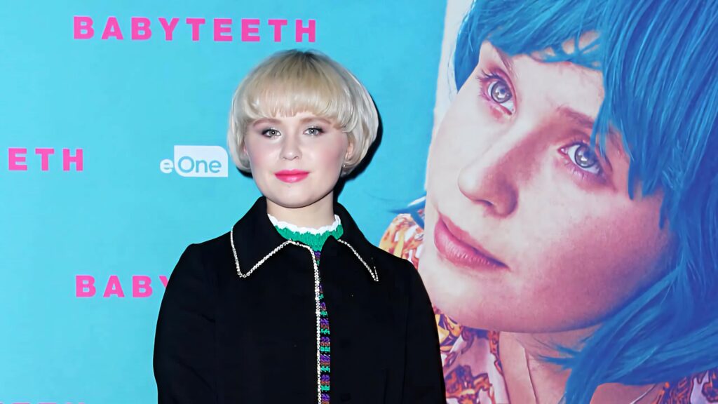 Eliza Scanlen as Milla Finlay with short blonde hair in black outfit on blue Babyteeth movie backdrop Wallpaper