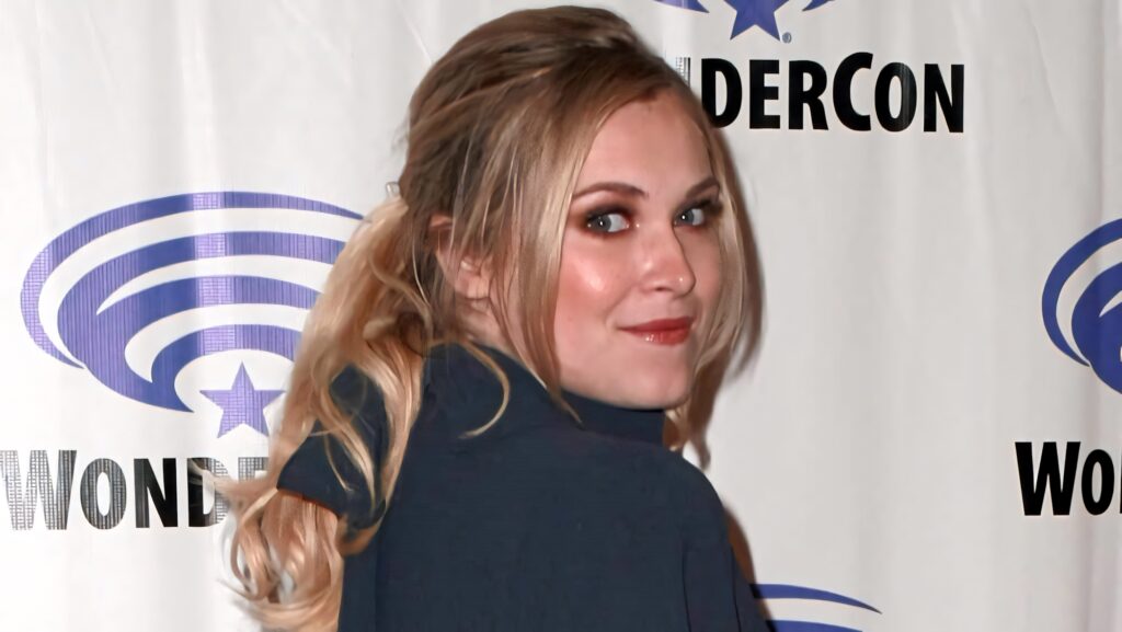 Eliza Taylor posing candidly at Wonder Con with branded backdrop and soft lighting highlights Wallpaper