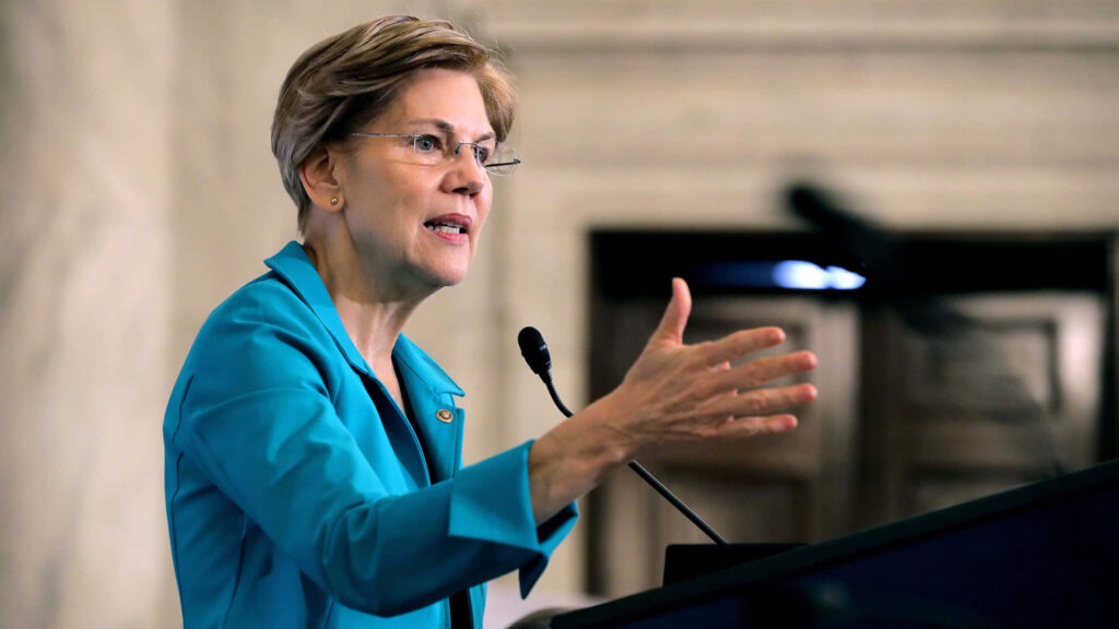 Elizabeth Warren speaking passionately at podium in turquoise blazer with blurred background wallpaper