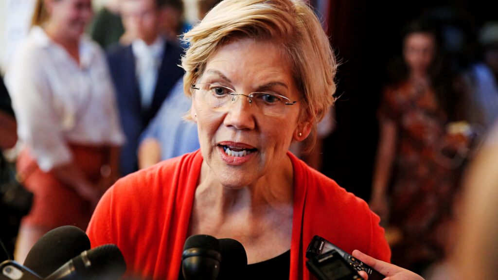 Elizabeth Warren mid-interview wearing red cardigan and glasses with microphones and journalists Wallpaper