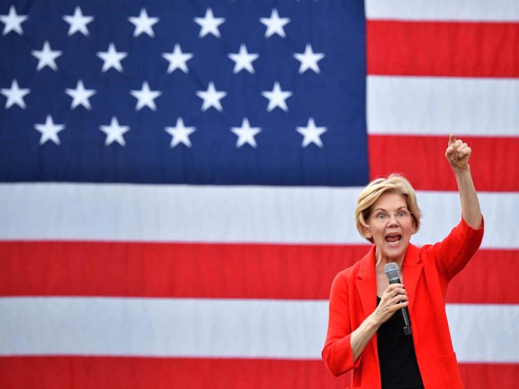 Elizabeth Warren speaking passionately with raised fist and microphone in front of American flag background Wallpaper