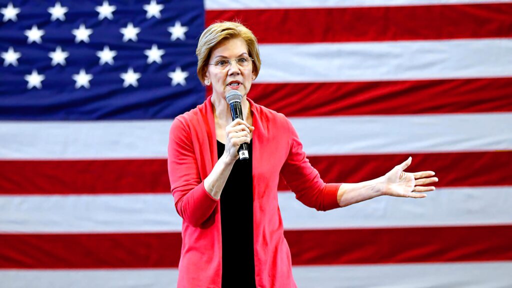 Elizabeth Warren speaking with microphone in front of large American flag patriotic political background Wallpaper