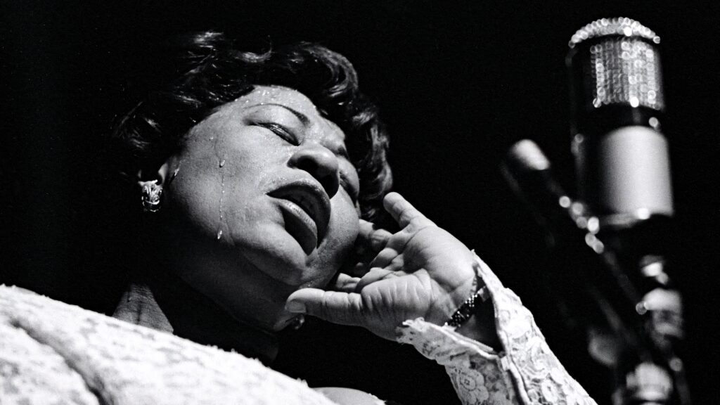 Low angle black and white wallpaper of Ella Fitzgerald singing soulful jazz with vintage microphone