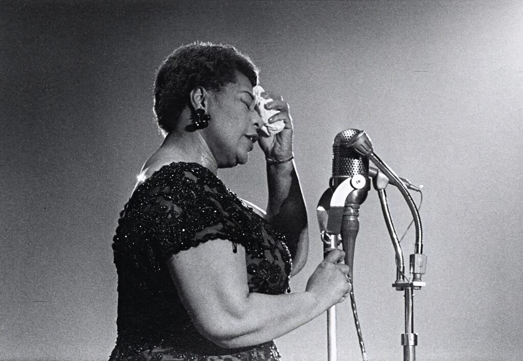 Ella Fitzgerald in shimmering gown singing by vintage microphone under dramatic stage lighting Wallpaper