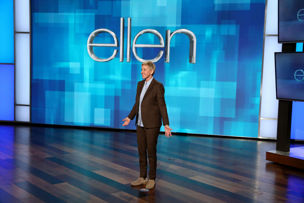 Ellen DeGeneres on vibrant blue stage with iconic ellen logo in lively talk show set background Wallpaper