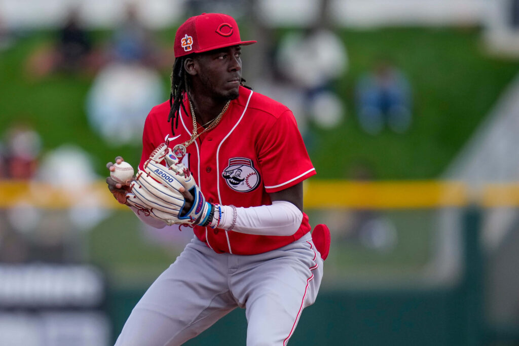Elly De La Cruz in red Cincinnati Reds jersey making a dynamic play on green baseball field Wallpaper