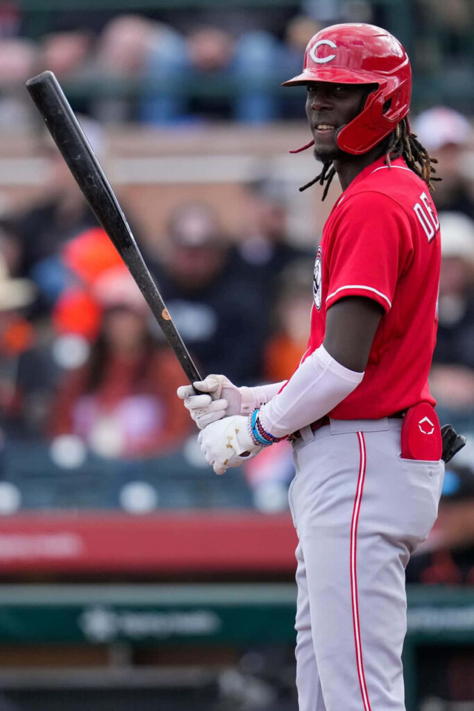 Elly De La Cruz in red Cincinnati Reds uniform batting with focus in blurred stadium background Wallpaper