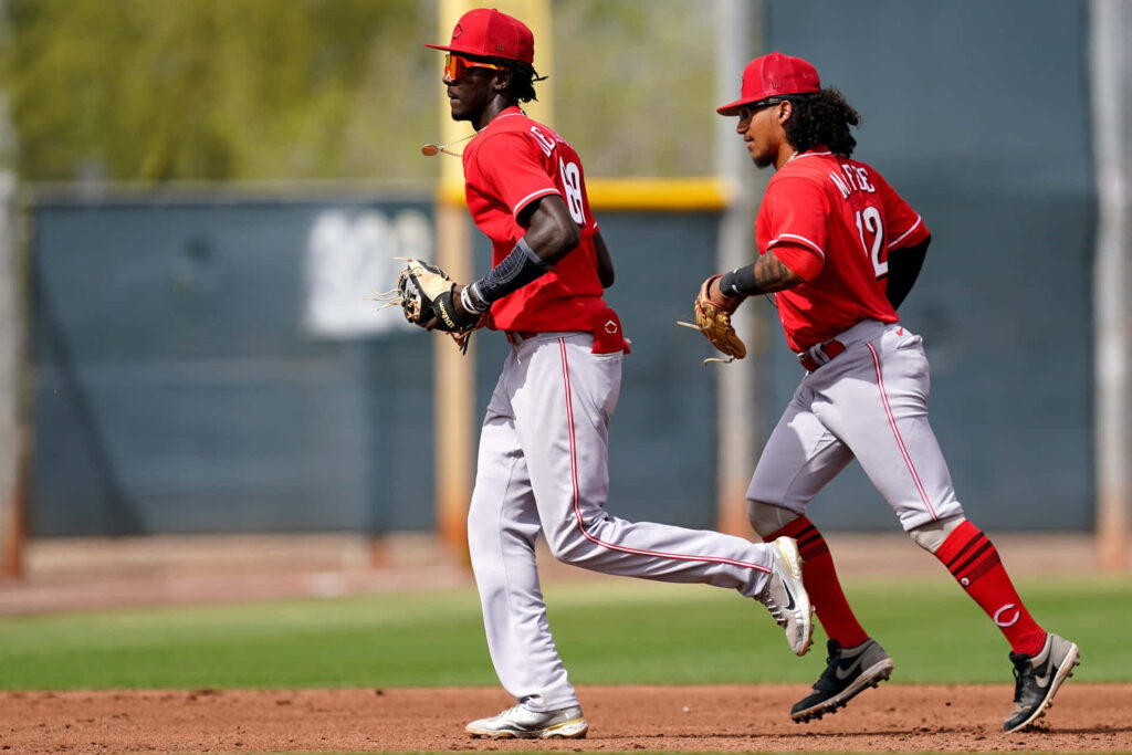 Elly De La Cruz and teammate sprinting in Cincinnati Reds uniforms dynamic baseball action wallpaper