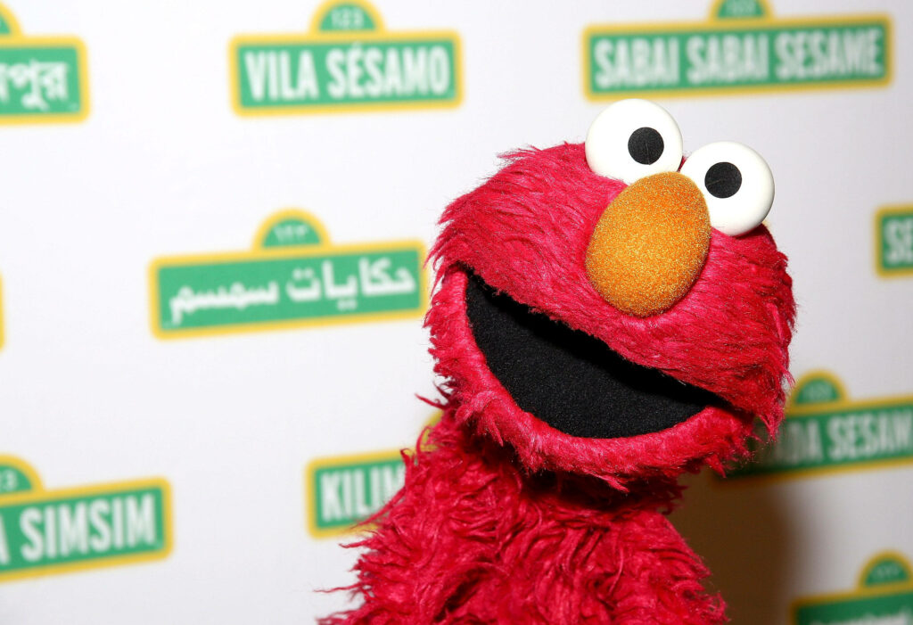 Elmo from Sesame Street with bright red fur and orange nose on colorful international logos wallpaper