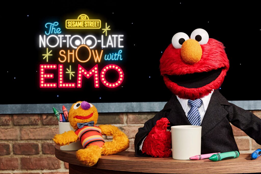 Elmo in suit hosting The Not Too Late Show with colorful Sesame Street inspired playful backdrop Wallpaper