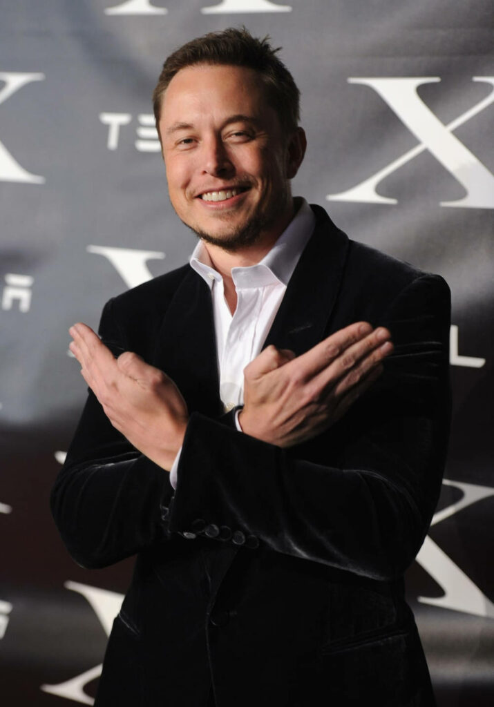 Elon Musk Wallpaper: Confident Pose with Tesla Logo Background
