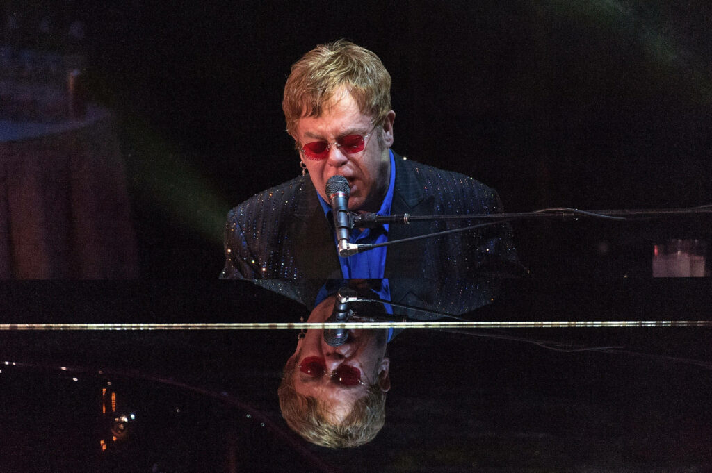 Elton John passionately plays piano wearing red sunglasses and sparkling jacket onstage concert Wallpaper