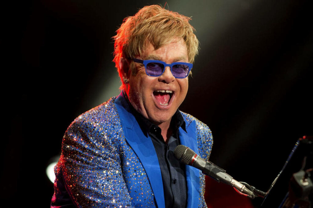 Elton John performing live in sparkling blue jacket and signature glasses vibrant stage lighting Wallpaper