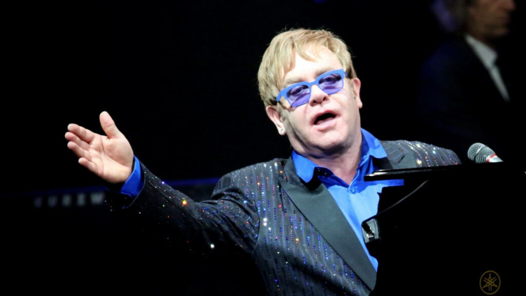 Elton John performing passionately at piano in sparkling jacket and signature tinted glasses Wallpaper