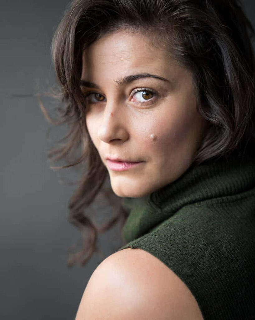 Portrait of Elysia Rotaru looking over shoulder with soft natural light and muted gray background Wallpaper