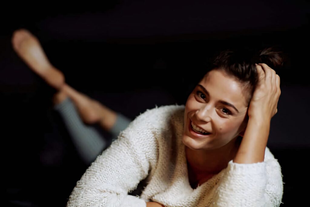 Elysia Rotaru smiling in textured white sweater with soft lighting dark blurred background portrait Wallpaper