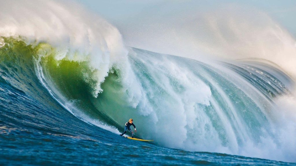 Young surfer on yellow board riding massive emerald green barrel wave ocean wallpaper background