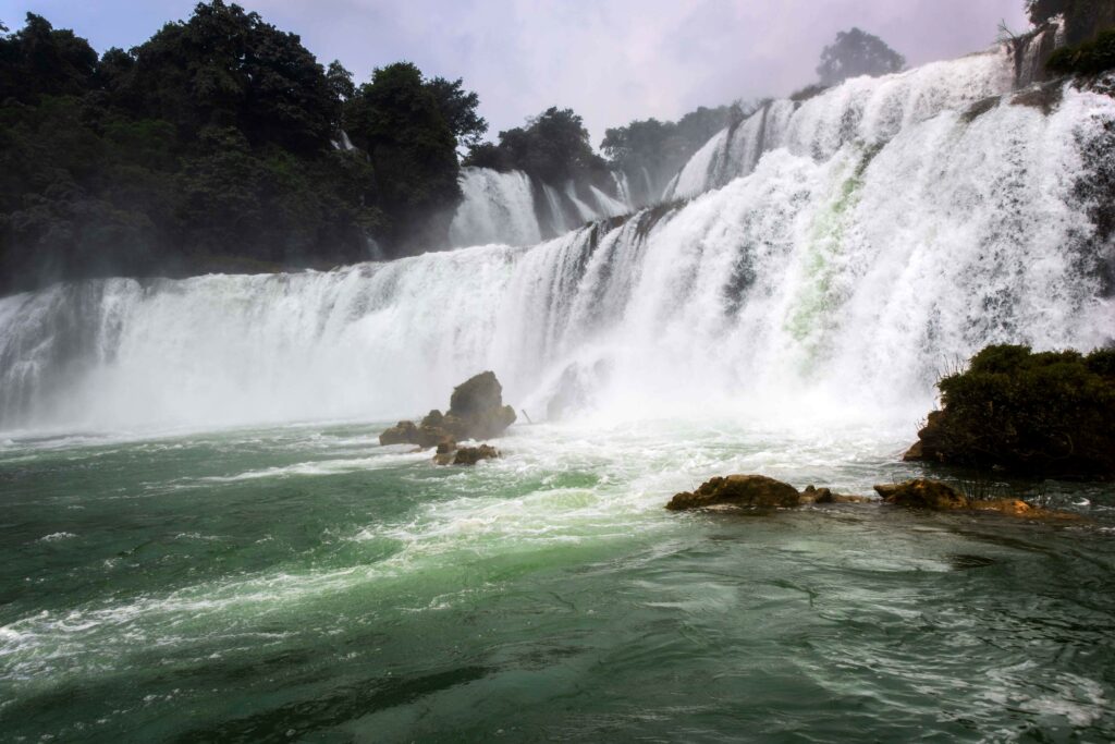 Waterfall cascading over rugged stones into emerald stream surrounded by lush green forest wallpaper
