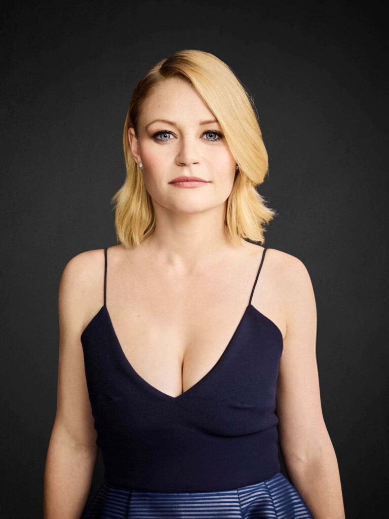 Emilie de Ravin in navy blue V-neck dress with sleek blonde hair on dark textured wallpaper background