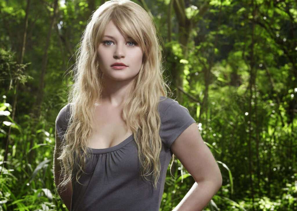 Emilie de Ravin in sunlit forest with blonde hair gray top lush green background serene wallpaper