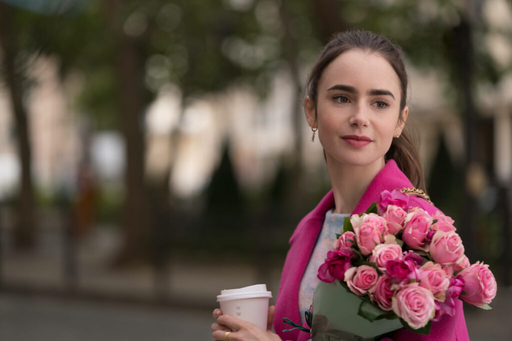 Emily Bloom in Paris walking with pink roses and coffee wearing vibrant pink coat city background Wallpaper