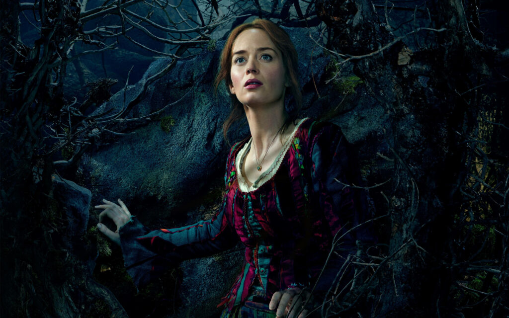 Emily Blunt as Into The Woods character standing in dark forest with twisted tree branches wallpaper