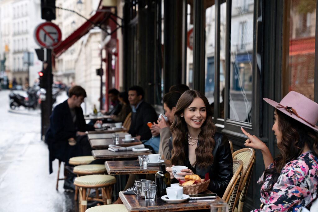 Emily enjoying tea at a charming Parisian café vibrant stylish Emily In Paris wallpaper background