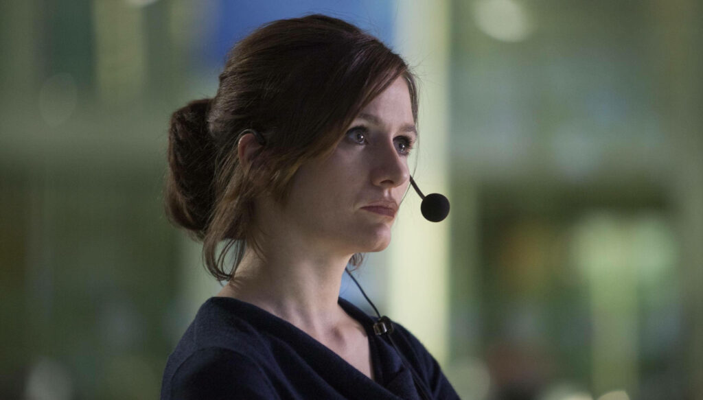 Emily Mortimer in modern softly lit workspace wearing discreet headset calm professional wallpaper