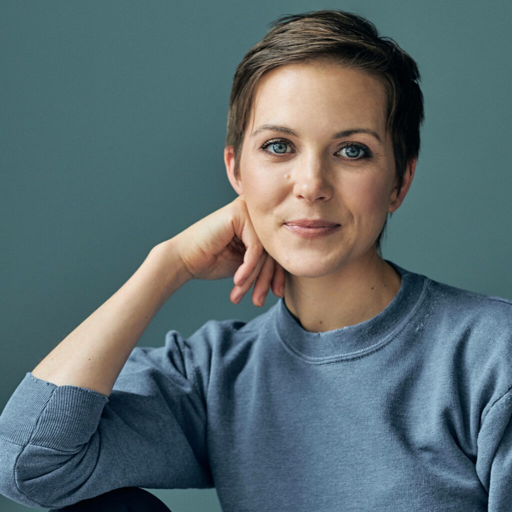 Portrait of author Emily Watson with expressive blue eyes on a muted teal wallpaper background