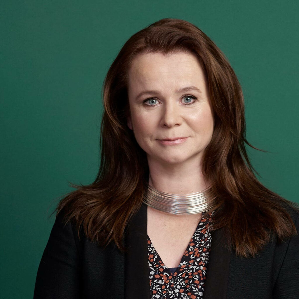 Emily Watson in modern black blazer and silver necklace against solid green minimalist backdrop Wallpaper