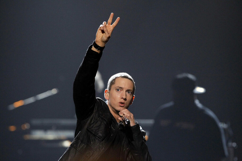Eminem on stage in black jacket showing peace sign dark concert background wallpaper