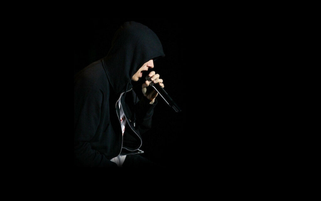 Eminem performing live in black hoodie passionately rapping into microphone on dark background Wallpaper