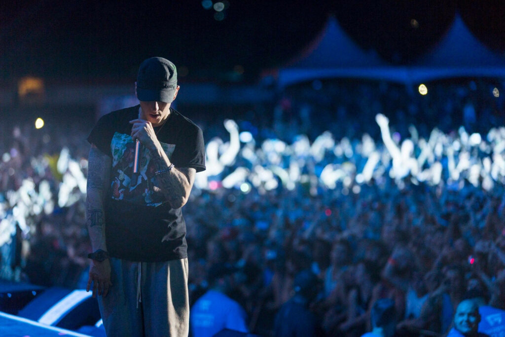 Eminem passionately performing on stage with vibrant lights and enthusiastic concert crowd background Wallpaper