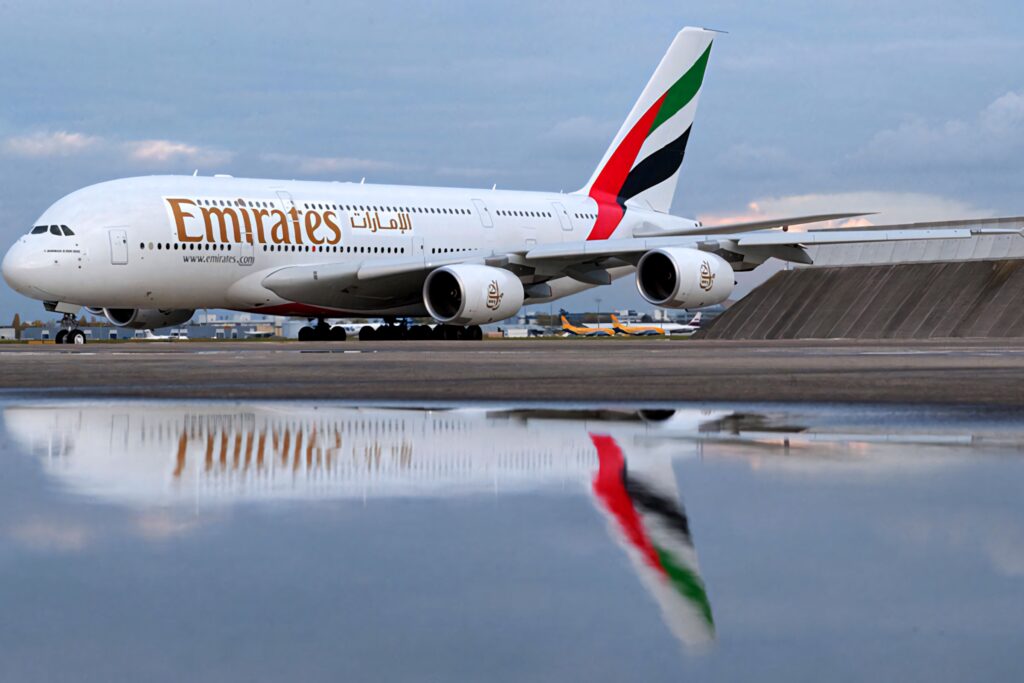 Emirates A380 on runway with sleek white fuselage and red green tail reflected in water pool Wallpaper