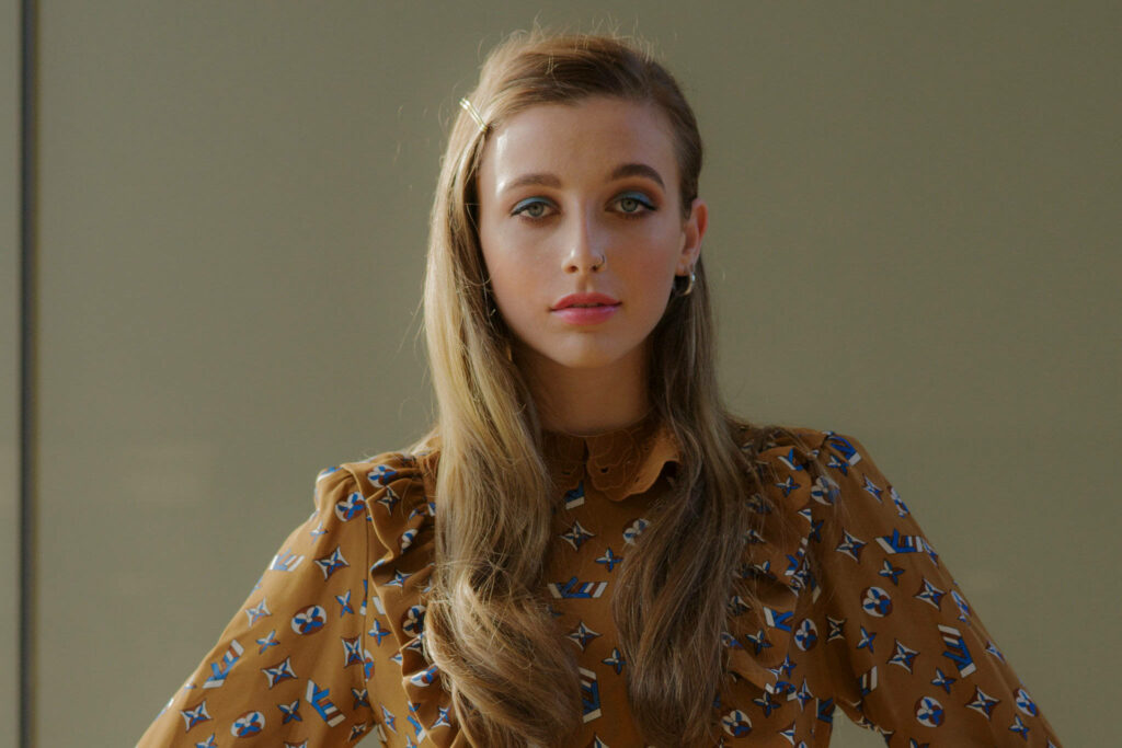 Emma Chamberlain wearing retro brown patterned blouse and classic hair clip with soft lighting Wallpaper