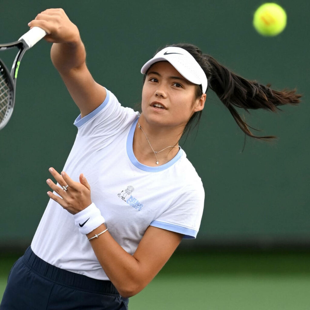 Emma Raducanu in white Nike visor and wristband focused mid-match on tennis court background Wallpaper