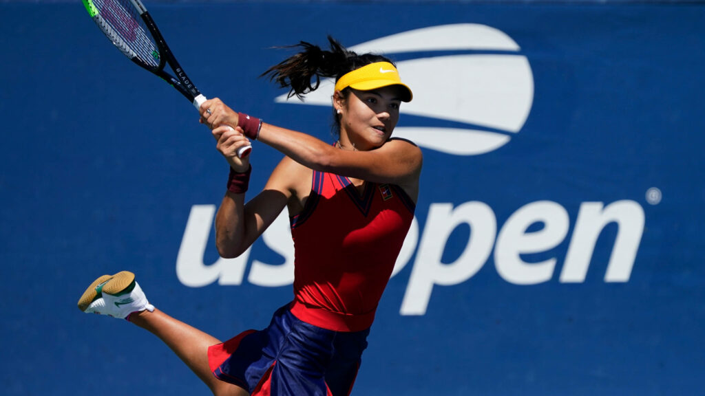 Emma Raducanu mid-swing US Open vibrant red navy tennis outfit yellow visor athletic action shot Wallpaper
