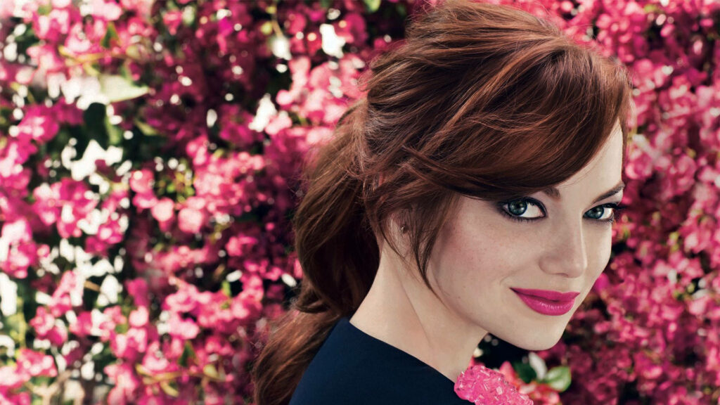 Emma Stone with green eyes and soft makeup poses before vibrant pink flowers in high-resolution wallpaper