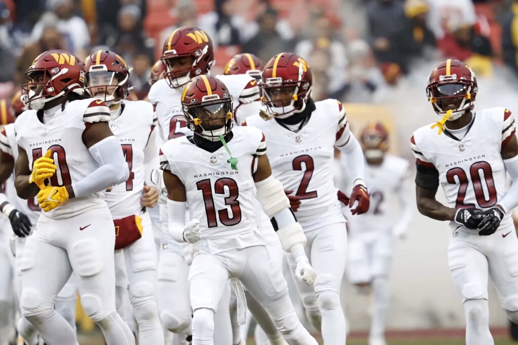 Emmanuel Forbes Jr and football team in white uniforms defending on field with blurred stadium background Wallpaper