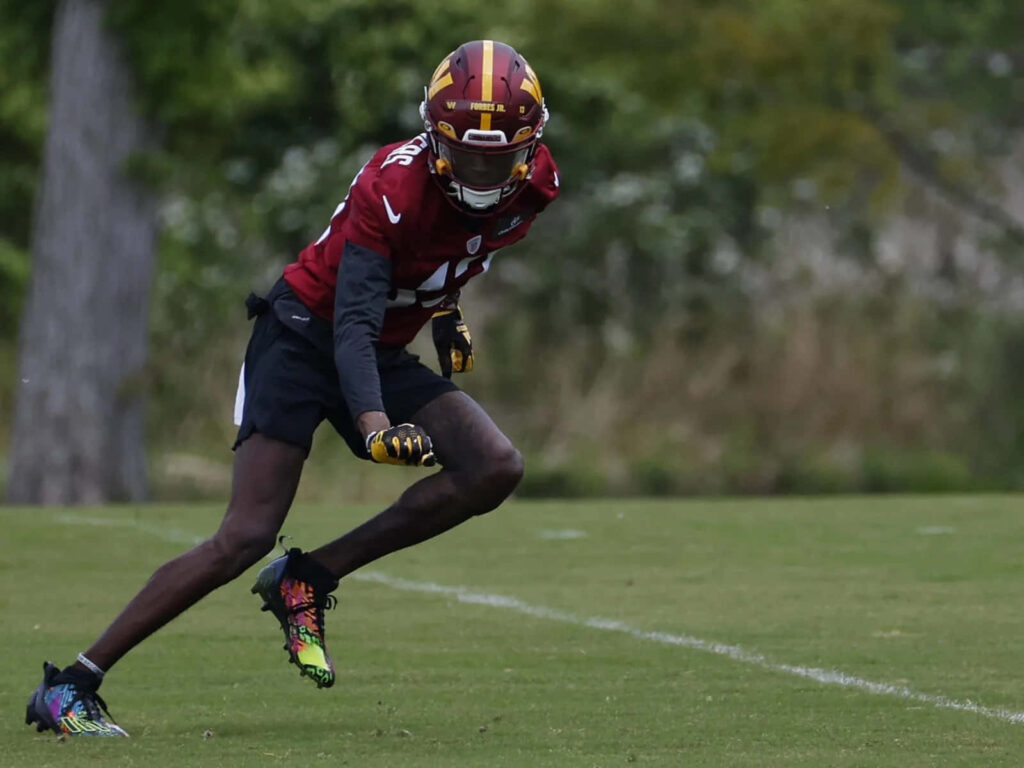 Emmanuel Forbes Jr agile mid action football drill in maroon gold jersey on green field background Wallpaper