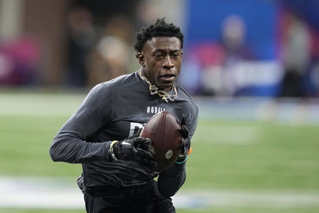 Emmanuel Forbes Jr mid game gripping football with intense focus on vibrant field background Wallpaper