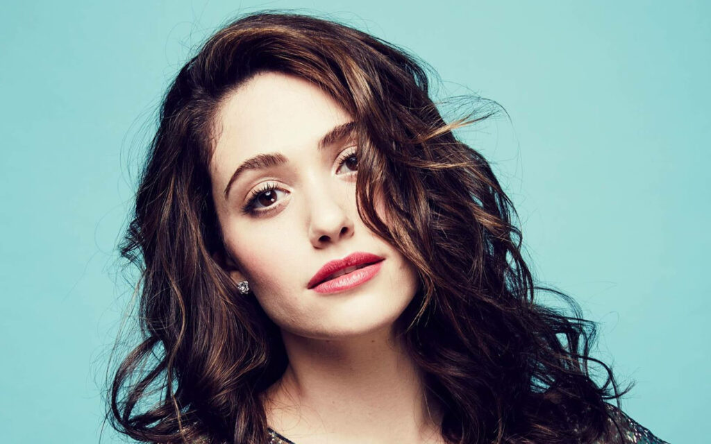 Emmy Rossum close-up portrait with wavy brown hair radiant skin expressive eyes blue background Wallpaper