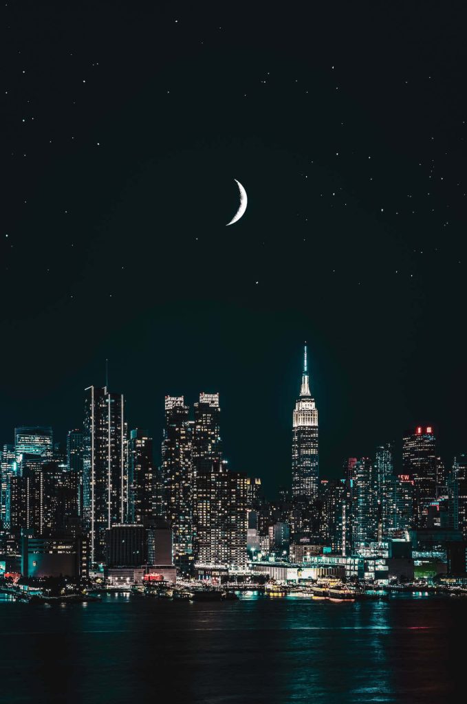 Empire State Building glowing at night with NYC skyline under crescent moon starry sky wallpaper
