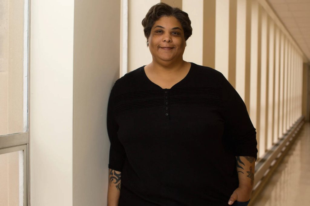 Confident plus-size woman with tattoos smiles in sunlit hallway portrait inspiring desktop wallpaper