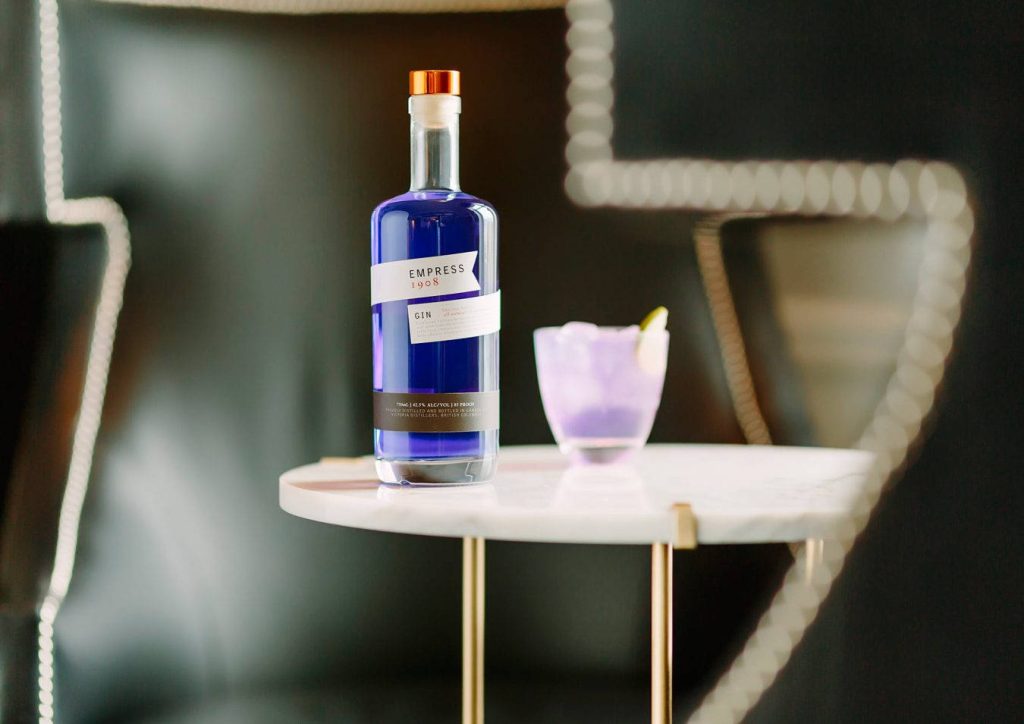 Elegant Empress 1908 Indigo Gin bottle with vibrant cocktail on marble table dark background Wallpaper