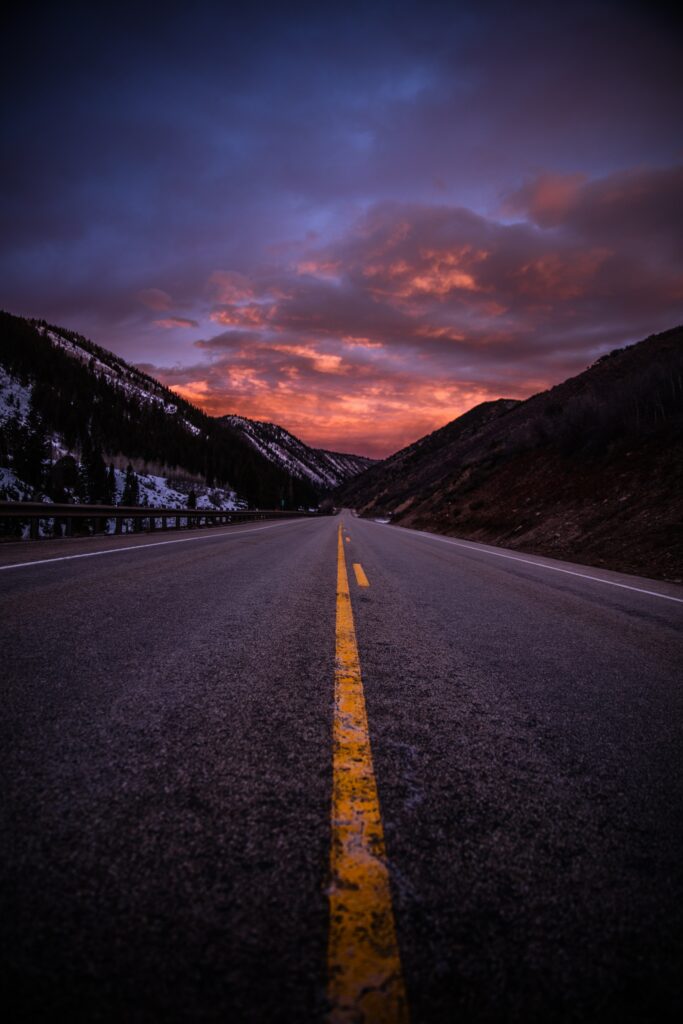 Empty road with yellow lines leading through rugged mountains under a vibrant evening sky wallpaper