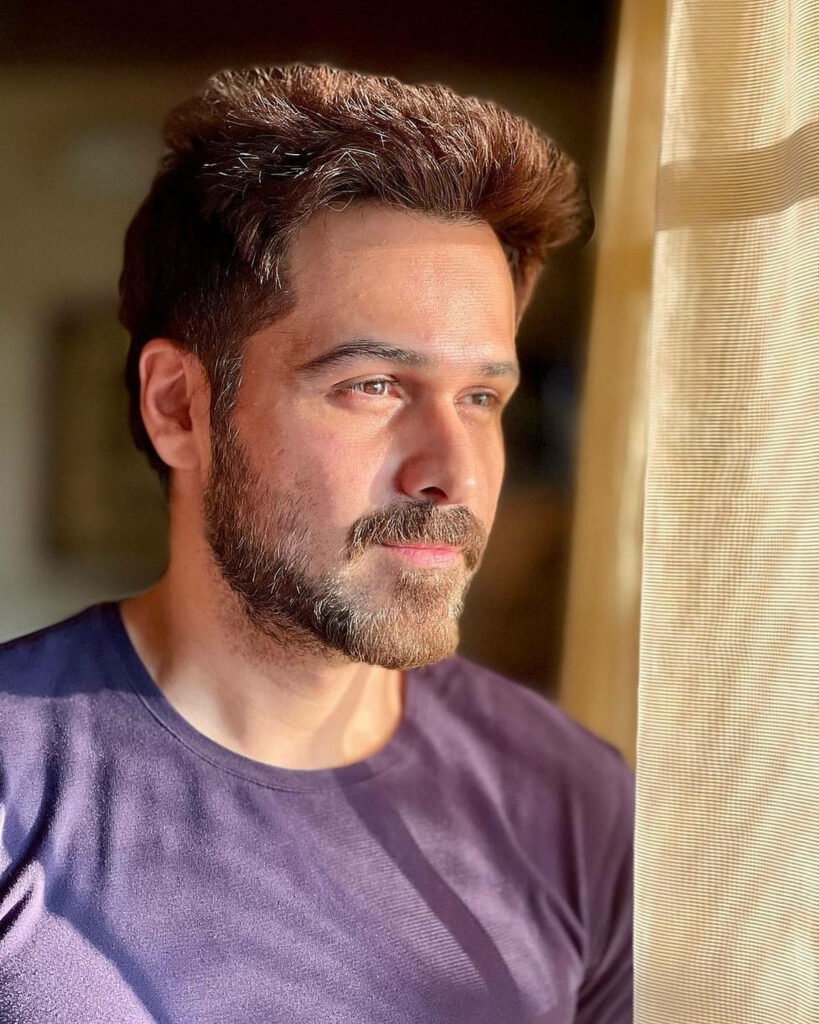 Emraan Hashmi in soft natural light with brown hair and beard wearing dark t-shirt looking thoughtful Wallpaper
