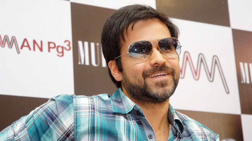 Emraan Hashmi wearing aviator sunglasses and checked blue shirt smiling against modern background Wallpaper